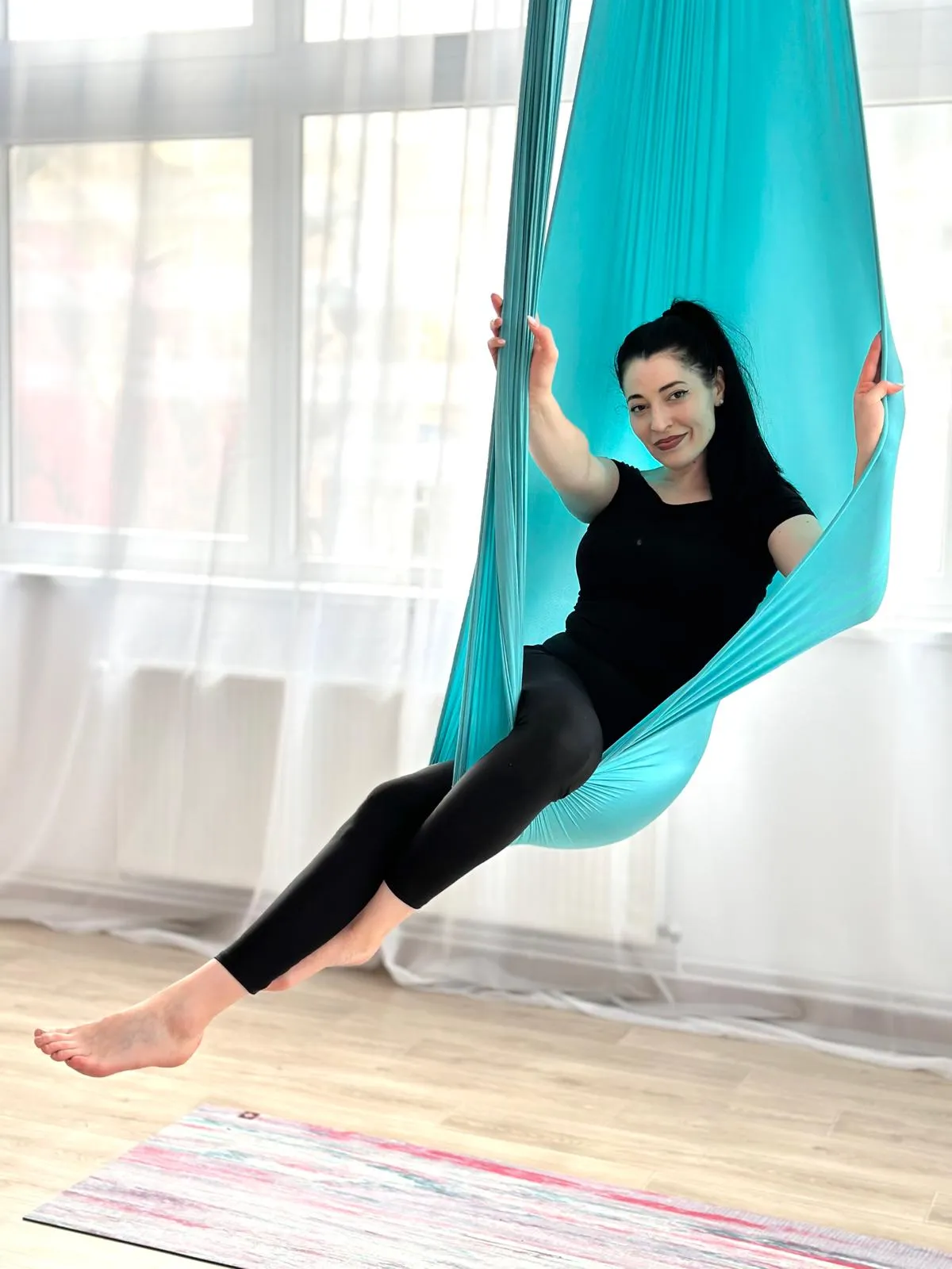 Andreea, instructor de Yin Aerial Yoga în Cluj-Napoca, așezată în hamacul turcoaz din studio